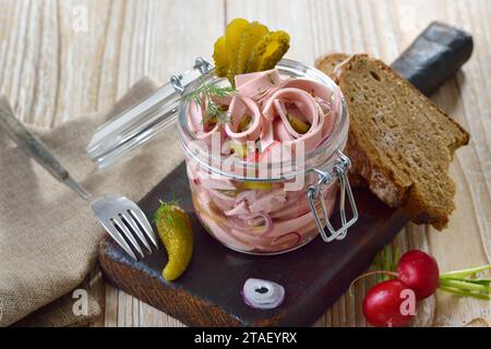 Herzhafter bayerischer Wurstsalat, serviert in einem Glas auf einem alten Holzschneidebrett Stockfoto