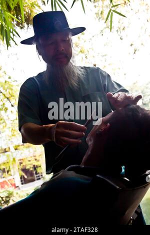 Ein Straßenfriseur schneidet einem Kunden in Hanoi, Vietnam, die Haare Stockfoto