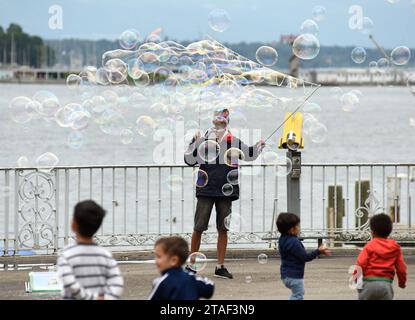 Genf, Schweiz - 05. Juni 2017: Straßenkünstler, der riesige Seifenblasen am See macht und Kinder versuchen, sie zu schnappen, Genf, Schweiz. Stockfoto