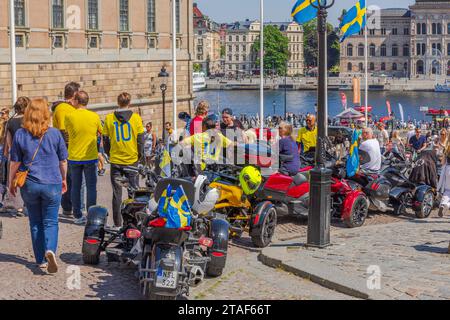 Blick auf eine Gruppe von Radfahrern auf dreirädrigen motorisierten Fahrzeugen, die sich auf dem Platz vor dem Königspalast in Stockholm versammeln, um Schwedens Nationalmannschaft zu feiern Stockfoto