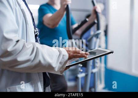 Nahaufnahme eines Arztes, der den Arztbericht auf Tablette mit Labormantel und Stethoskop in einer Klinik überprüft. Kaukasischer Arzt surft im Internet, während er ein digitales Gerät hält. Stockfoto