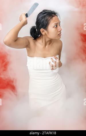 Eine junge Frau, die in weißem Rauch steht, ist mit einem Messer bewaffnet Stockfoto