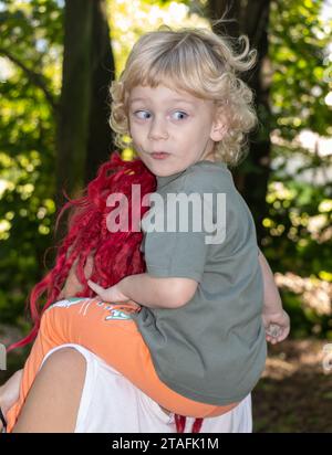 Eine Mutter trägt ihren Sohn auf ihren Schultern, der grimmig wird, als er sich umdreht Stockfoto