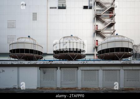 Große Kühlanlage und Lüftungseinheiten auf dem Dach des Lagers mit schließenden Rollladentüren und Hintergrund des weißen Gebäudes. Stockfoto