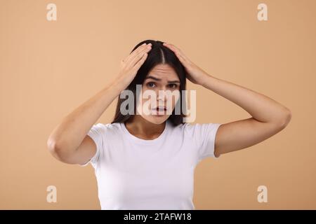 Emotionale Frau, die ihr Haar und ihre Kopfhaut auf beigefarbenem Hintergrund untersucht Stockfoto