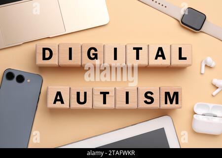 Phrase Digital Autismus aus Holzwürfeln und Geräten auf beigefarbenem Hintergrund, flache Lage. Suchtverhalten Stockfoto