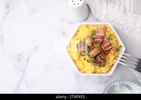 Gekochtes Maismehl mit Speck, Pilzen und Mikrogrün in Schüssel auf weißem Marmortisch, Blick von oben. Leerzeichen für Text Stockfoto