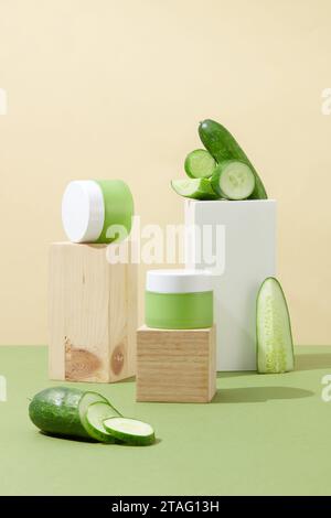 Gläser mit Gurkenextrakt-Lotion werden auf Holzplattformen platziert, einige Gurken werden auf einem hohen weißen Podium platziert. Minimalistischer Hintergrund für Kosmetik Stockfoto