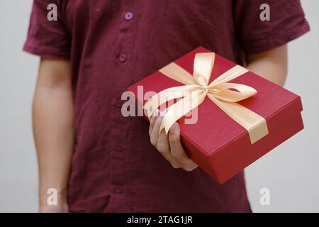 Männliche Hände halten eine kleine rote Geschenkbox, umwickelt mit goldenem Band. Nahaufnahme und Innenaufnahme. Selektiver Fokus. Weihnachtskonzept. Stockfoto