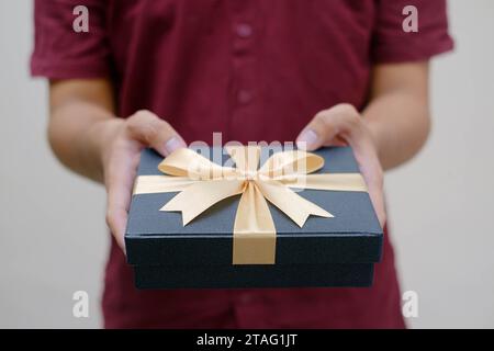 Männliche Hände, die eine kleine Geschenkbox mit goldenem Band halten. Nahaufnahme und Innenaufnahme. Selektiver Fokus. Weihnachtskonzept. Stockfoto