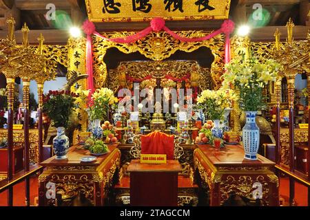 Farbenfroher Blick auf den Hauptaltar in einem buddhistischen Tempel in Hanoi, Vietnam. Blumen, Obst, Süßigkeiten und Bier gehören zu den Opfergaben an die Gottheiten Stockfoto