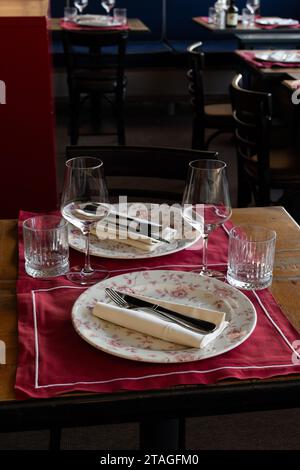 Ein kleiner Holztisch für zwei Gäste ist elegant mit Tellern, Gläsern, Besteck, Gabel und Messer sowie Servietten in einem kleinen Café in Florenz, Italien, eingerichtet. Stockfoto