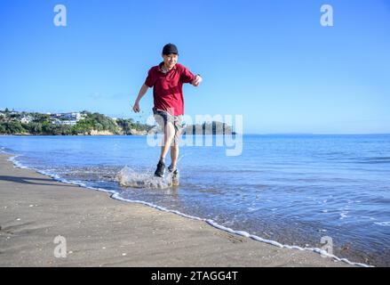 Mann, der im Wasser am Milford Beach läuft. Auckland. Stockfoto