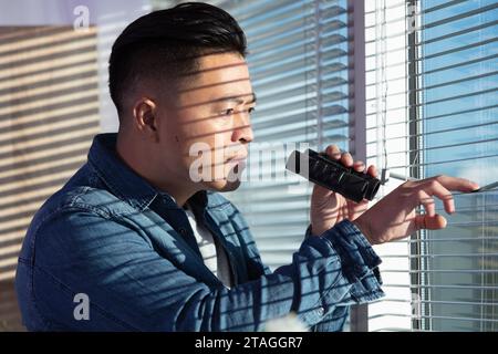 Mann, der durch Fensterläden mit Fernglas schaut Stockfoto