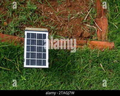 Kleines tragbares Solarzellenmodul auf dem Rasen mit Schotterland und rotem Backstein im Hintergrund, saubere Energie für die Stromerzeugung im Haus Stockfoto