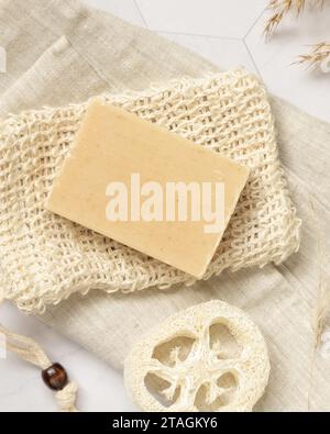 Beige Seifenstange auf Seifensparbeutel in der Nähe von natürlichem Schwamm auf weißem Marmor, Blick von oben, Verpackungsmodell, Kopierraum. Natürliches pflanzliches Produkt für Gesicht und Körper Stockfoto