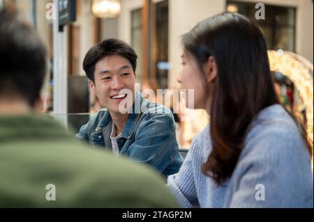 Ein fröhlicher junger asiatischer Mann, der es genießt, mit seinen Freunden zu reden, während er am Wochenende zusammen in einem Café in der Stadt abhängt. Freunde und Lifestyle Co Stockfoto