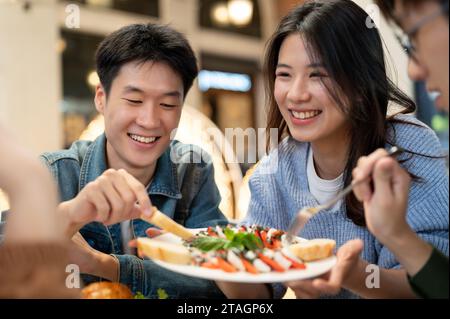 Eine Gruppe fröhlicher und fröhlicher junger asiatischer Freunde genießt gemeinsam Essen in einem Restaurant, hängt ab und genießt ein tolles Mittagessen. Personen und f Stockfoto