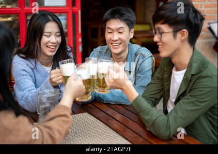 Eine Gruppe fröhlicher und fröhlicher junger asiatischer Freunde jubelt, toast, klirrt oder genießt am Wochenende ein Bier in einem Restaurant oder einer Bar in der Stadt Stockfoto
