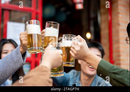 Eine Gruppe fröhlicher junger asiatischer Freunde jubelt, toast, klirrt oder trinkt gemeinsam ein Bier in einem Restaurant oder einer Bar in der Stadt. L Stockfoto