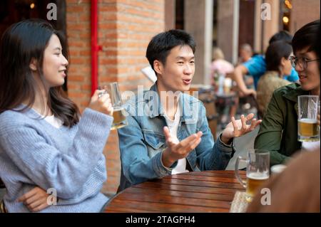 Ein glücklicher junger asiatischer Mann erzählt seine lustige Geschichte, während er mit seinen Freunden in einer Bar Bier genießt. Party, Happy Moment, Bier Moment, ich Stockfoto