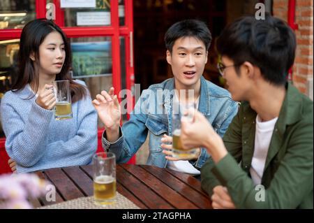 Ein glücklicher junger asiatischer Mann erzählt seine lustige Geschichte, während er mit seinen Freunden in einer Bar Bier genießt. Party, Happy Moment, Bier Moment, ich Stockfoto