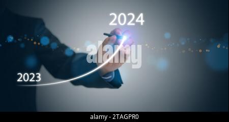 Ein Geschäftsmann zeichnet auf virtuellen technischen Bildschirmen eine steigende Kurve, von Ende 2023 bis Anfang 2024. Wir freuen uns über ein frohes neues Jahr und freuen uns auf ein neues Geschäftsziel Stockfoto