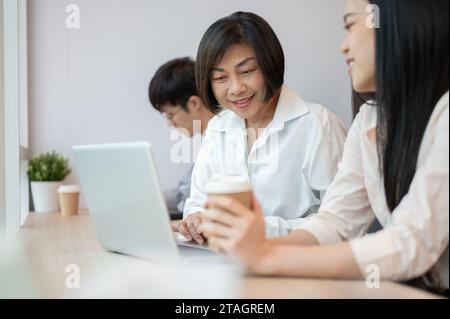 Eine glückliche und freundliche asiatische Geschäftsfrau spricht und arbeitet mit einer jungen Kollegin im Büro. Vielseitiges Konzept für Geschäftsleute Stockfoto
