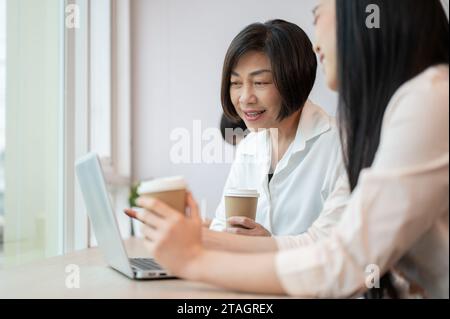 Eine glückliche und freundliche asiatische Geschäftsfrau spricht und arbeitet mit einer jungen Kollegin im Büro. Vielseitiges Konzept für Geschäftsleute Stockfoto
