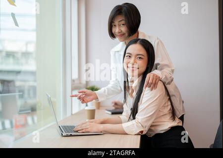 Eine professionelle und freundliche asiatische Chefin hilft und coacht ein neues Projekt für eine junge Kollegin, die gemeinsam im Büro arbeitet. Stockfoto