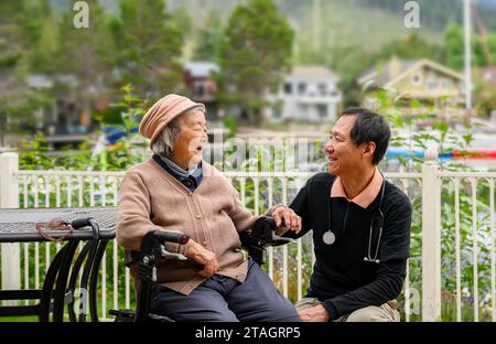 Männlicher Arzt besucht Seniorinnen zu Hause. Patient sitzt auf dem Gehhilfen im Garten. Stockfoto