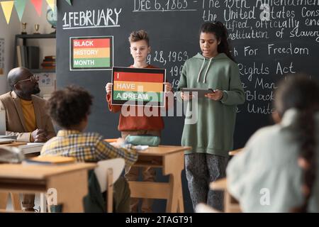 Schulkinder stehen neben der Tafel und halten während eines Unterrichts Vorträge für Klassenkameraden und Lehrer im Klassenzimmer Stockfoto