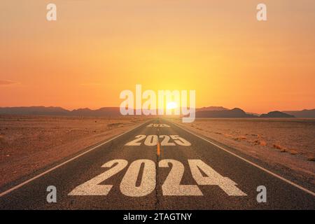 Neujahr 2024 oder einfaches Konzept. Text 2024 auf der Straße in der Mitte der Asphaltstraße bei Sonnenuntergang geschrieben. Konzept der Planung, des Ziels, der Herausforderung Stockfoto