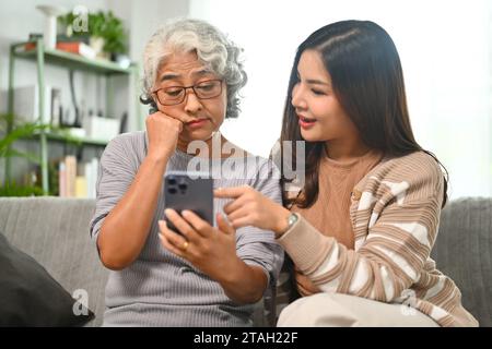 Junge Frau unterrichtet reife Mutter über soziale Netzwerke auf dem Handy. Ältere Menschen und Technologiekonzept Stockfoto