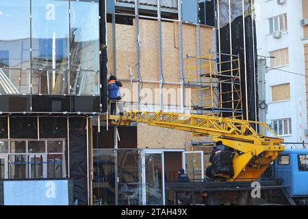 Nicht exklusiv: CHARKIW, UKRAINE - 30. NOVEMBER 2023 - Ein Bauarbeiter ersetzt zertrümmerte Fenster durch Spanplatten an einem Bürogebäude Stockfoto