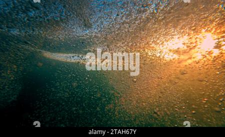 Unterwasseraufnahme der Sonnenstrahlen, die durch die Meereswellen strahlen. Luftblasen steigen auf. Stockfoto
