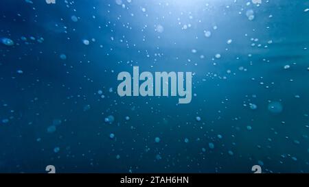 Unterwasseraufnahme von Sonnenstrahlen, die durch klares Meerwasser mit aufsteigenden Luftblasen scheinen. Stockfoto