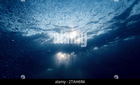Blick vom Meeresboden auf Sonnenstrahlen, die durch die Wasseroberfläche strahlen. Aufsteigende Luftblasen funkeln und glitzern im Licht. Stockfoto