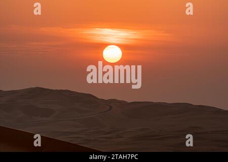 Sonnenaufgang über den Sanddünen mit einer leeren Straße am Horizont, trübem Himmel. Stockfoto