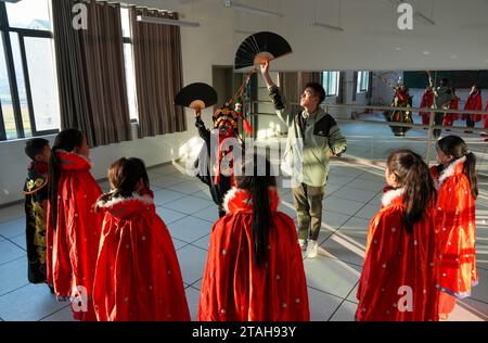 Chongqing, Chinas Chongqing. November 2023. Der Volkskünstler Li Yong demonstriert Gesten des traditionellen „bian lian“ oder Gesichtswandlungsfähigkeiten in der Wu'an Grundschule im Bezirk Dianjiang, im Südwesten Chinas Chongqing, 28. November 2023. Mit mehr als 600 Schülern kooperierte die Wu'an Grundschule in den letzten Jahren mit dem Volkskünstler Li Yong und fügte Gesichtswechsel als besonderen Teil ihres Lehrplans hinzu. Die Technik des Gesichtswechsels ist einer der berühmtesten Teile der Sichuan Opera, bei der Schauspieler schnell ihr Gesicht in atemberaubender und dramatischer Wirkung verändern. Quelle: Liu Chan/Xinhua/Alamy Live News Stockfoto