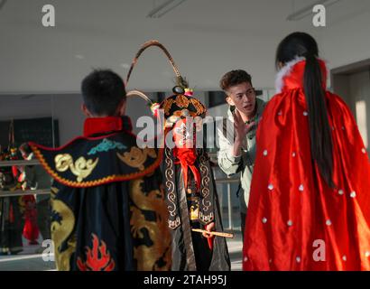 Chongqing, Chinas Chongqing. November 2023. Der Volkskünstler Li Yong (2. R) erklärt am 28. November 2023 die traditionelle „bian lian“, oder Gesichtswechsel, an der Wu'an Grundschule im Bezirk Dianjiang im Südwesten Chinas in Chongqing. Mit mehr als 600 Schülern kooperierte die Wu'an Grundschule in den letzten Jahren mit dem Volkskünstler Li Yong und fügte Gesichtswechsel als besonderen Teil ihres Lehrplans hinzu. Die Technik des Gesichtswechsels ist einer der berühmtesten Teile der Sichuan Opera, bei der Schauspieler schnell ihr Gesicht in atemberaubender und dramatischer Wirkung verändern. Quelle: Liu Chan/Xinhua/Alamy Live News Stockfoto