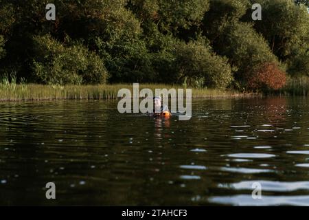 Professioneller Schwimmer in einem Neoprenanzug schwimmt im offenen Wasser auf einem See. Stockfoto