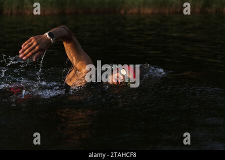 Professioneller Schwimmer in einem Neoprenanzug schwimmt im offenen Wasser auf einem See. Stockfoto