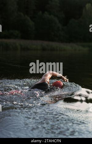 Professioneller Schwimmer in einem Neoprenanzug schwimmt im offenen Wasser auf einem See. Stockfoto