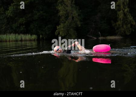 Professioneller Schwimmer in einem Neoprenanzug schwimmt im offenen Wasser auf einem See. Stockfoto