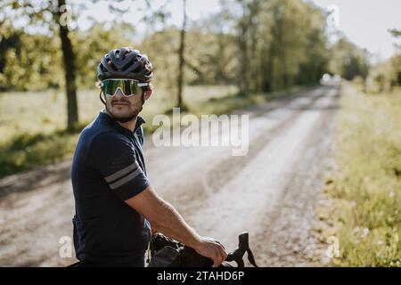 Radfahrer mit Helm und Sonnenbrille schaut die Schotterstraße hinunter Stockfoto