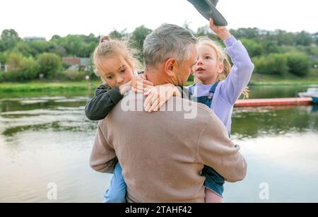 Vater trägt zwei Töchter in den Armen, wenn sie im Park spielen Stockfoto