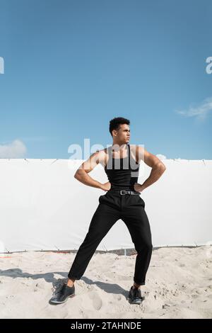 Starker kubanischer Mann in stilvollem schwarzem Outfit, der Hände an Hüften hält in Miami, South Beach Stockfoto