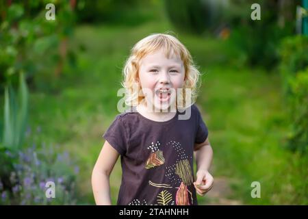 Kleines süßes kleines Mädchen, das im Park schreit und mit gedrehten Augen. Porträt eines süßen kleinen Mädchens im Garten an einem sonnigen Sommertag Stockfoto
