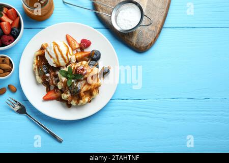 Köstliche belgische Waffeln mit Eis, Beeren und Karamellsauce serviert auf hellblauem Holztisch, flach gelegt. Leerzeichen für Text Stockfoto